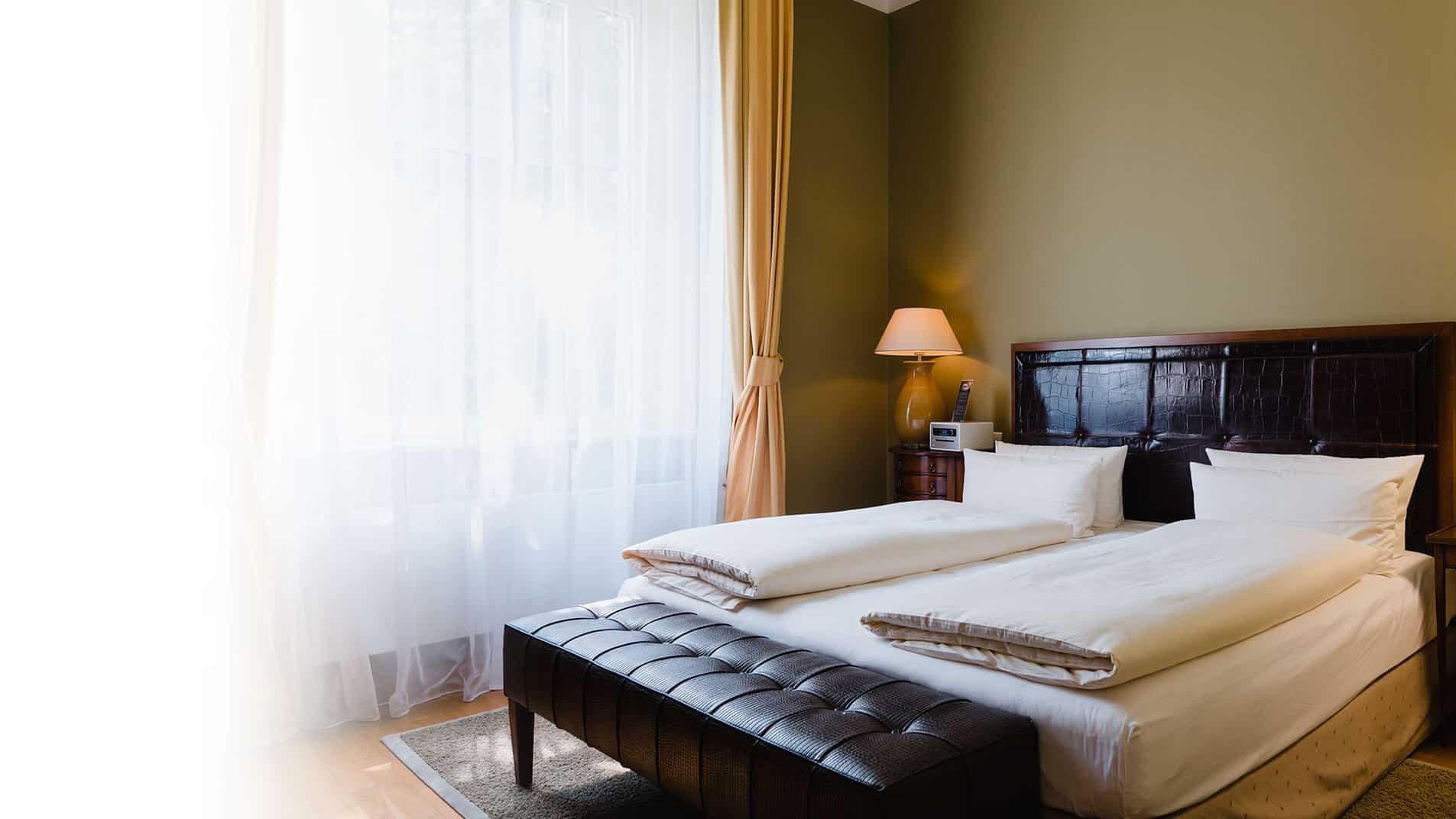 Gemachtes Bett in geschmackvoll eingerichtetem Superior Zimmer im Louisa's Place mit dunkelgrüner Wandfarbe und lederner Bettbank
