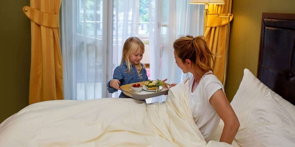 Mädchen bringt Frau ansprechend gedecktes Frühstückstablett ans Bett im Familienzimmer des Louisa's Place Hotel am Kudamm Berlin