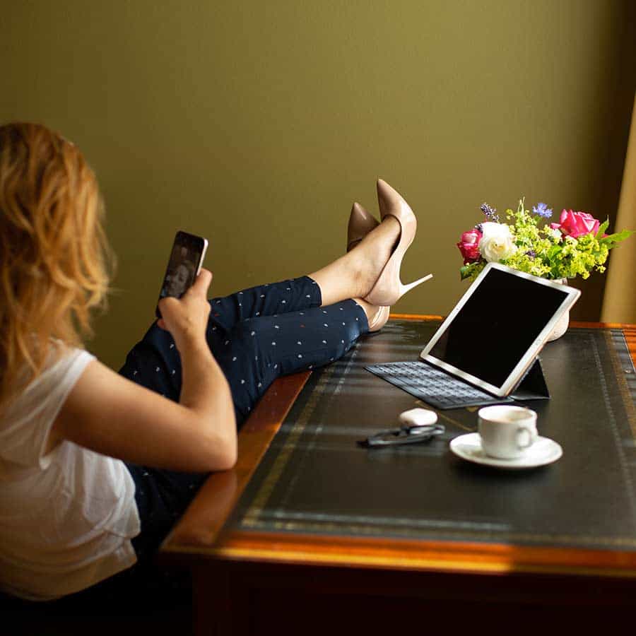 Frau sitz am Schreibtisch und checkt ihr Handy