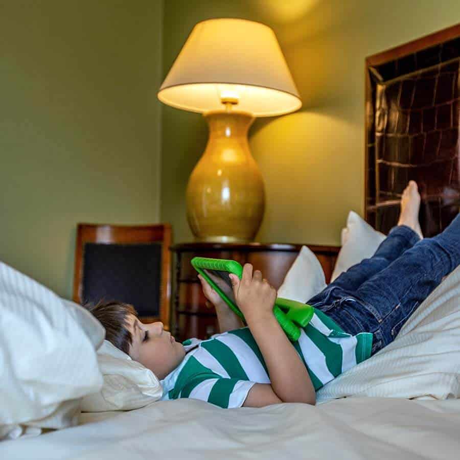 Junge liegt mit Tablet im gemütlichen Bett des Familienzimmers im Louisa's Place Hotel Kudamm Berlin