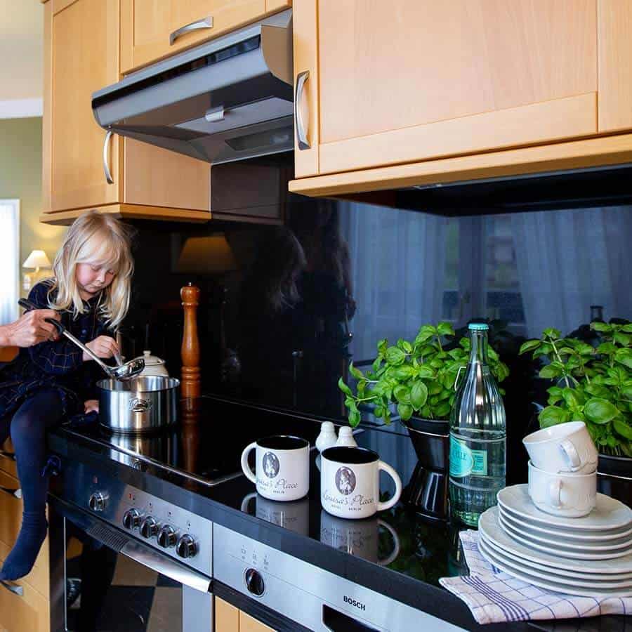 Vollausgestattete Küche der großzügigen Familienzimmer im Louisa's Place Hotel am Kudamm Berlin. Mädchen sitzt auf der Arbeitsplatte und rührt im Kochtopf um.