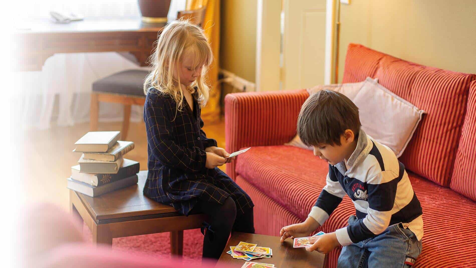 Mädchen und Junge spielen gemeinsam Karten im Wohnbereich des Familienzimmers im Louisa's Place Hotel