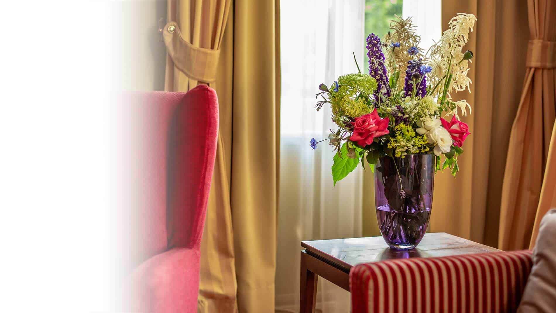 Farbenfroher Blumenstrauß in lila Glasvase auf einem Holztisch im Premium Zimmer des Louisa's Place