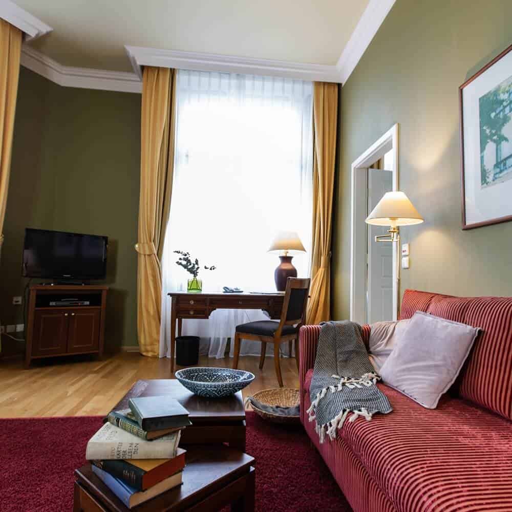 Gemütliches rotes Sofa mit Kissen und Decke und Flatscreen in der Louisa's Place Grand Suite