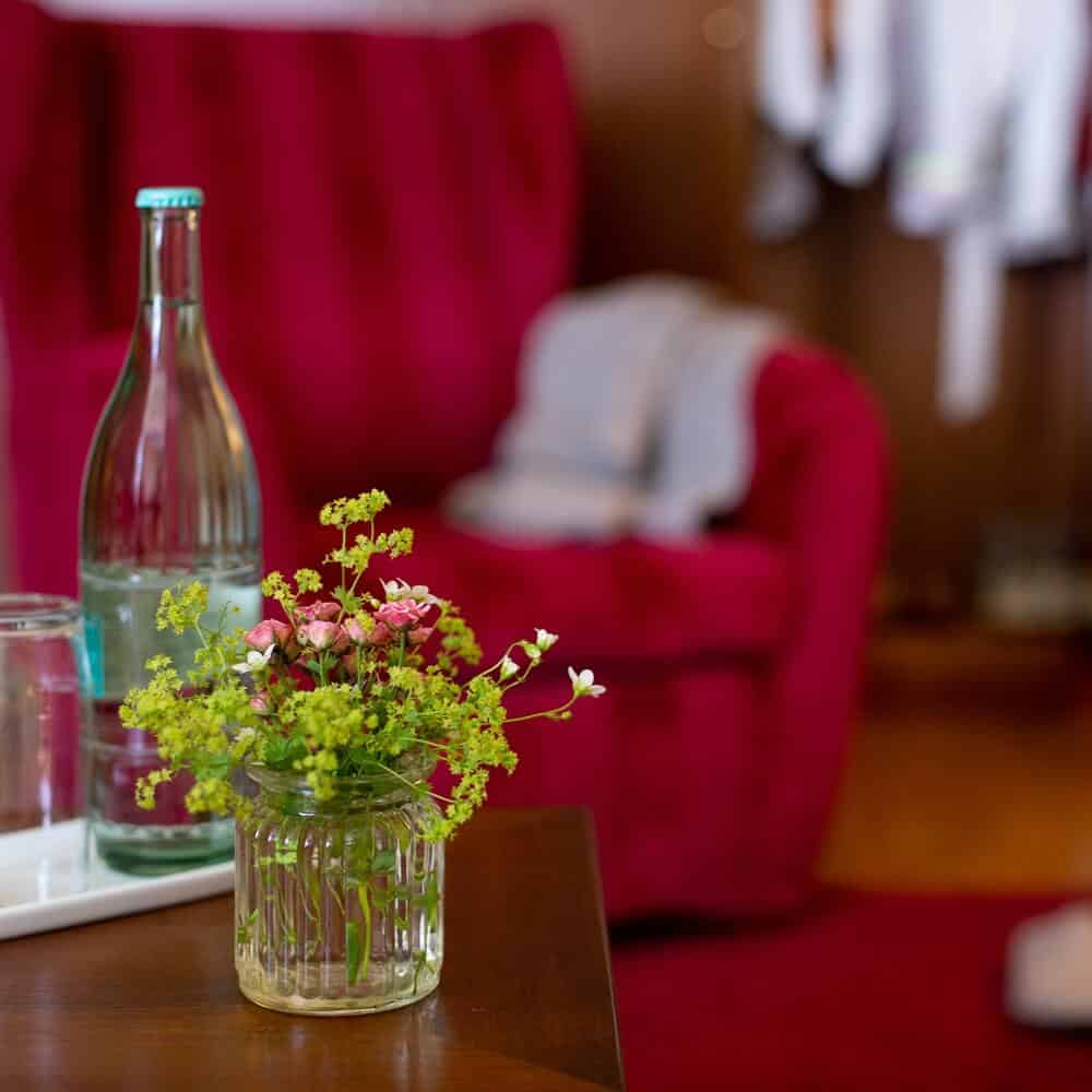 Wasserflasche und kleine Vase mit Blumen auf einem hölzernen Wohnzimmertisch in der Grand Suite des Louisa's Place Hotel.