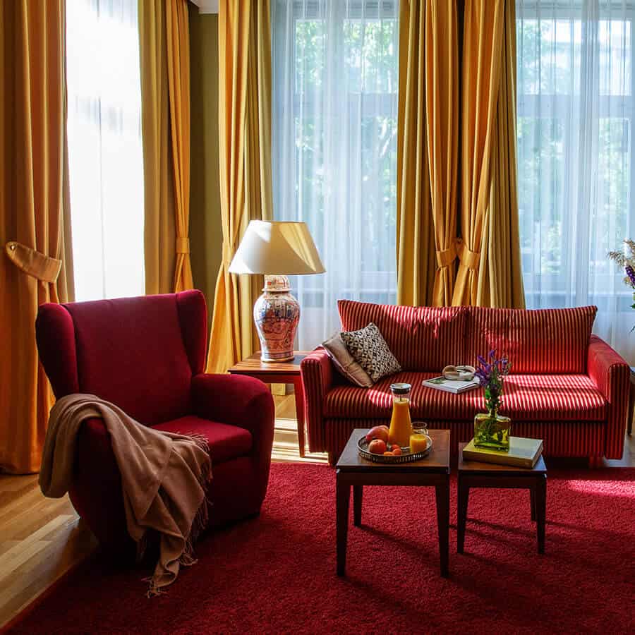 Sitzecke mit Sessel, Sofa und hölzernen Beistelltischen in Luisa's Suite im Boutiquehotel am Kudamm Berlin