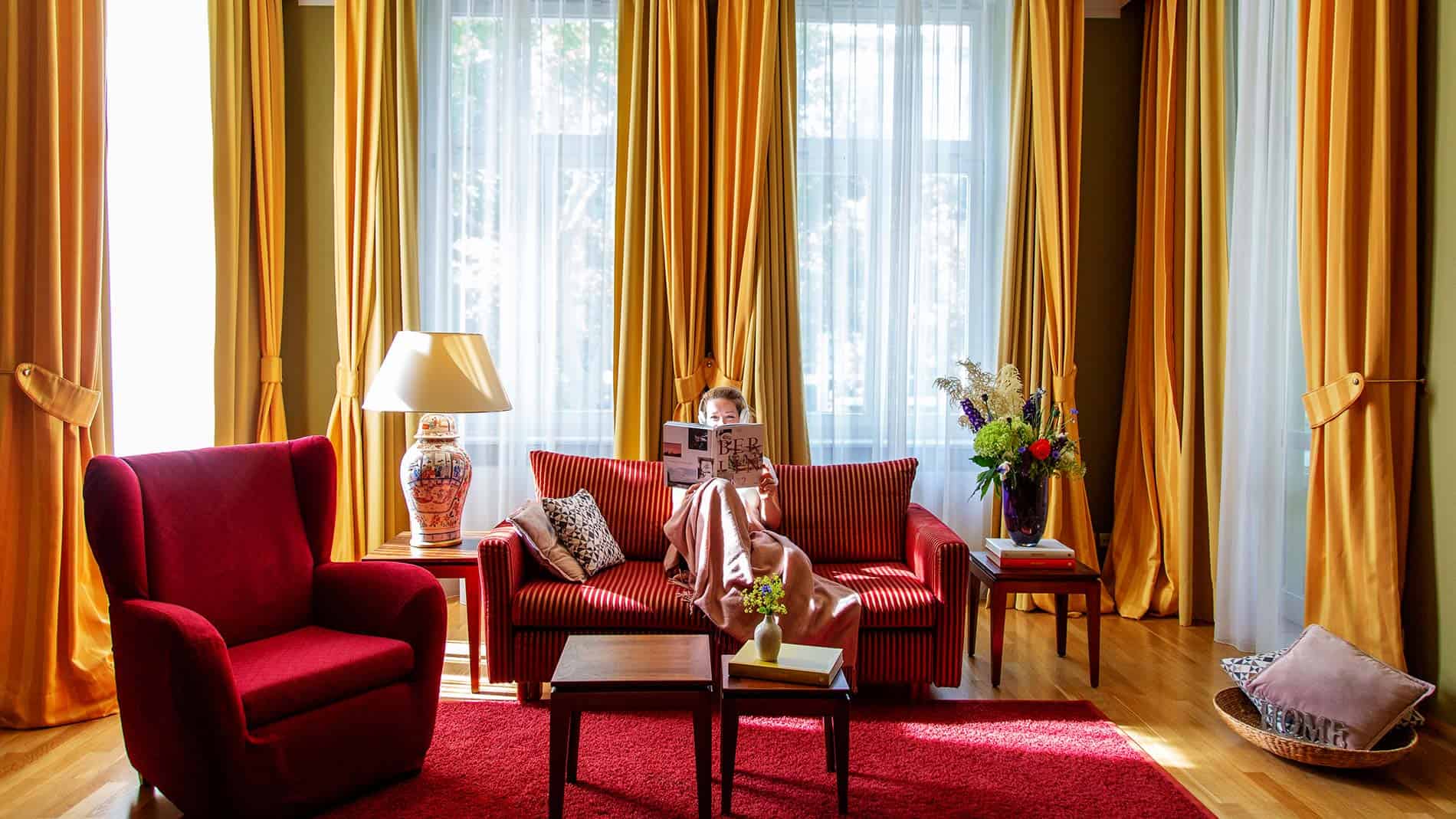 Eine Frau sitzt mit einer Decke auf dem Sofa und liest ein Magazin in der Grand Suite des Louisa's Place Hotel Berlin