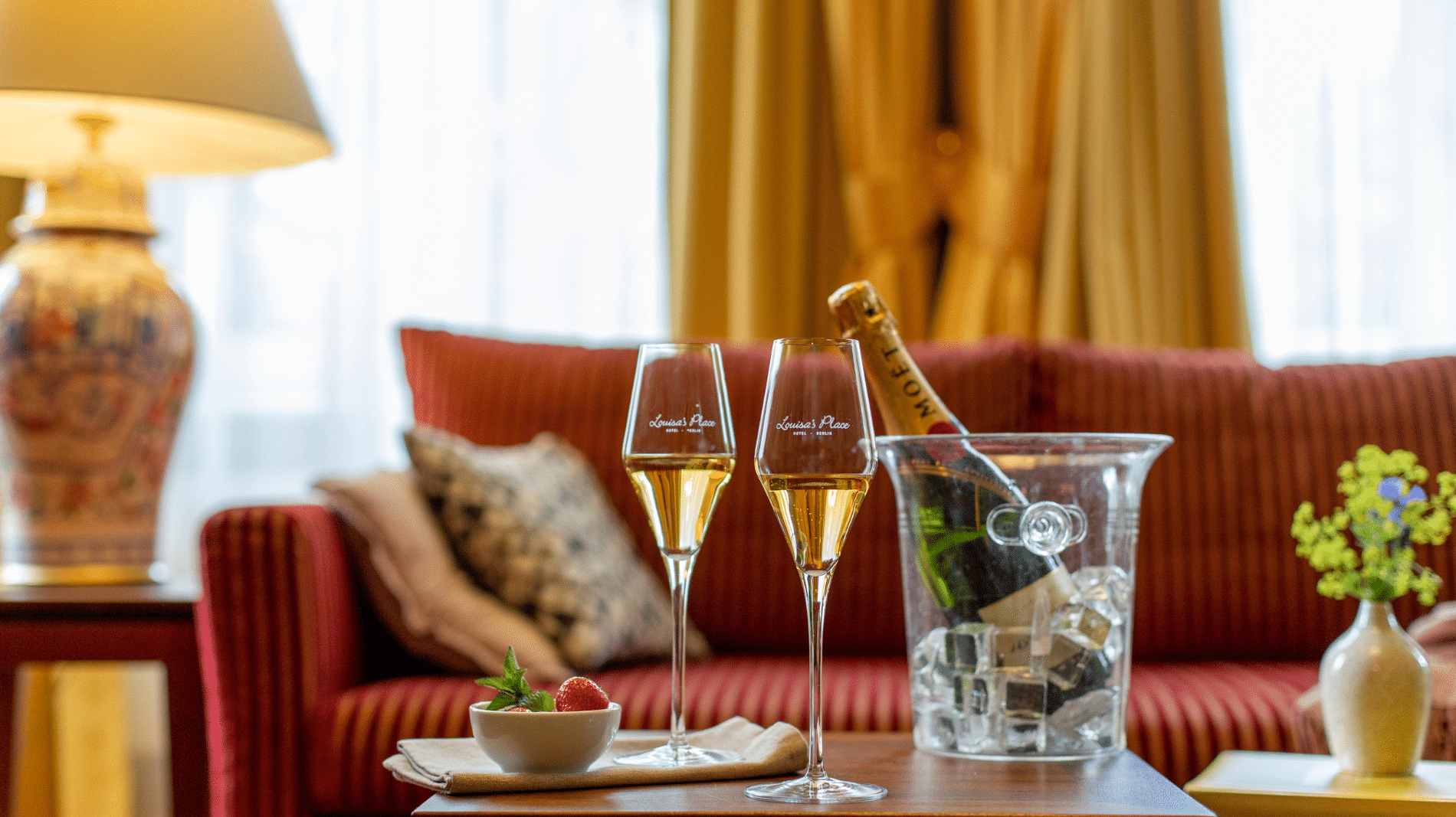 Zwei gefüllte Champagner Gläser steht angerichtet mit Erdbeeren und einem Champagner Kühler auf dem Tisch in einer Suite im Boutique Hotel Louisa´s Place in Berlin.