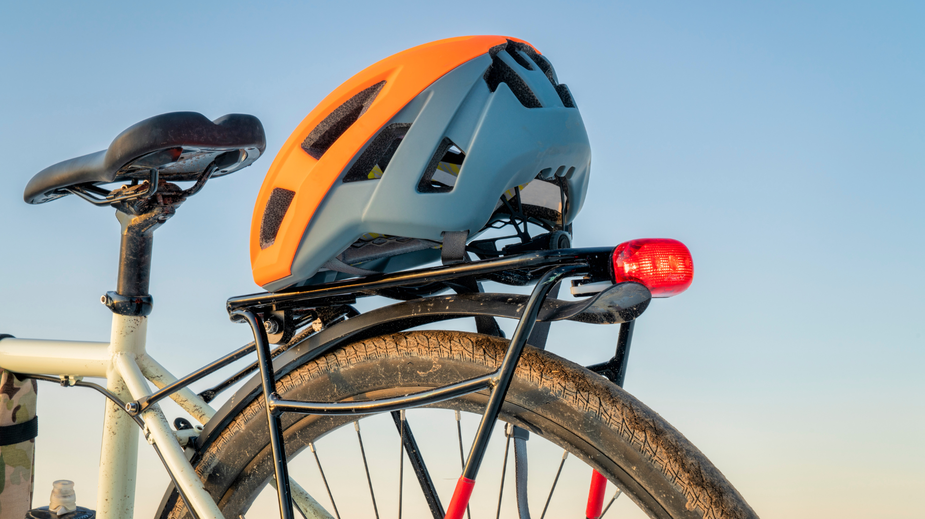 Orang-blauer Fahrradhelm liegt auf dem Gepäckträger eines weißen Fahrrads.