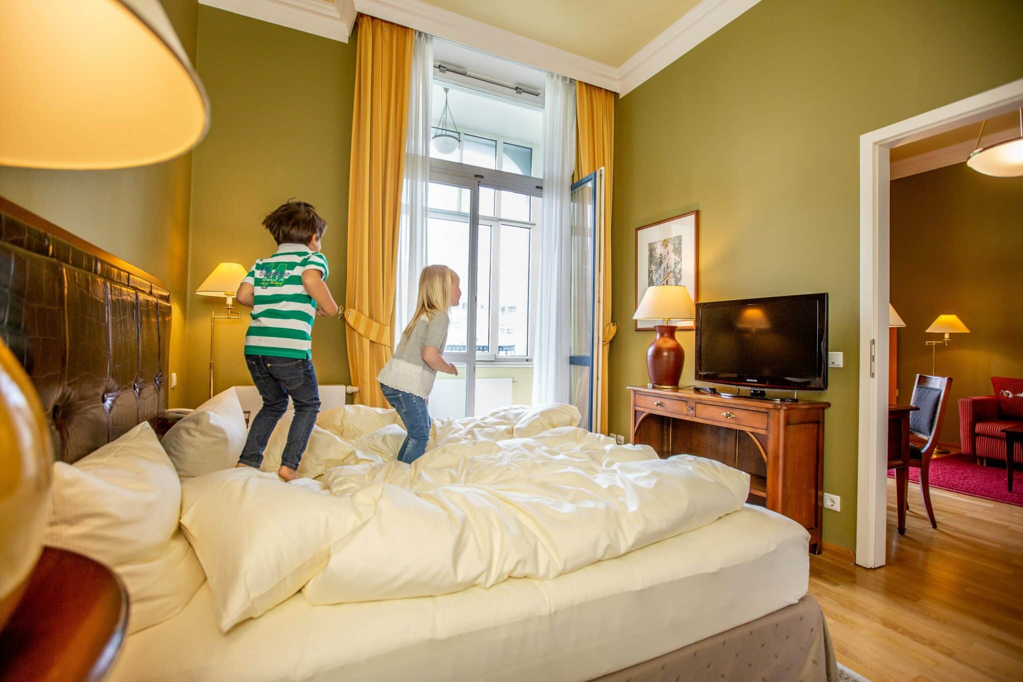 Ein kleiner Junge und ein kleines Mädchen springen spielend auf dem Bett im Familienzimmer des Louisa´s Place Hotel herum.